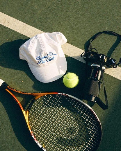 White hat with blue embroidery on tennis court and racket